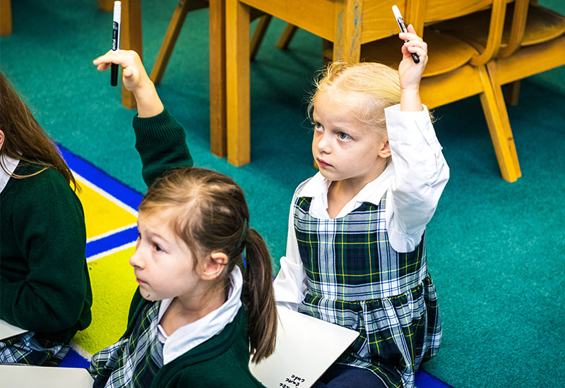 Reception girl putting hand up in class